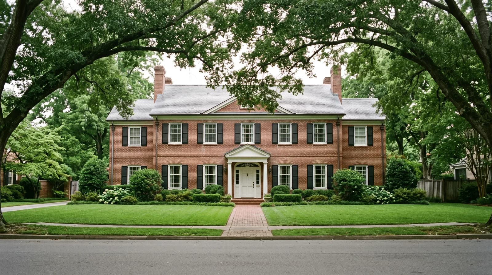 A 1930s red brick Georgian Colonial Revival house under mature willow oaks